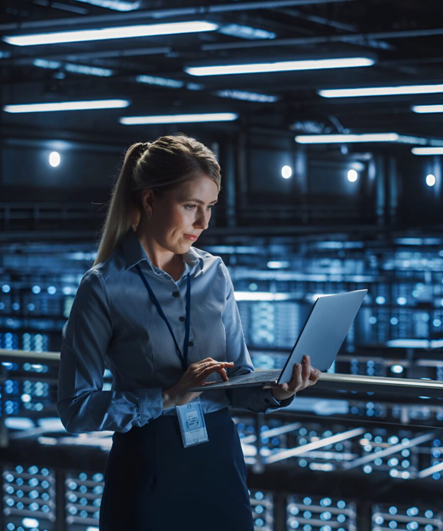 Woman working on laptop in server room.